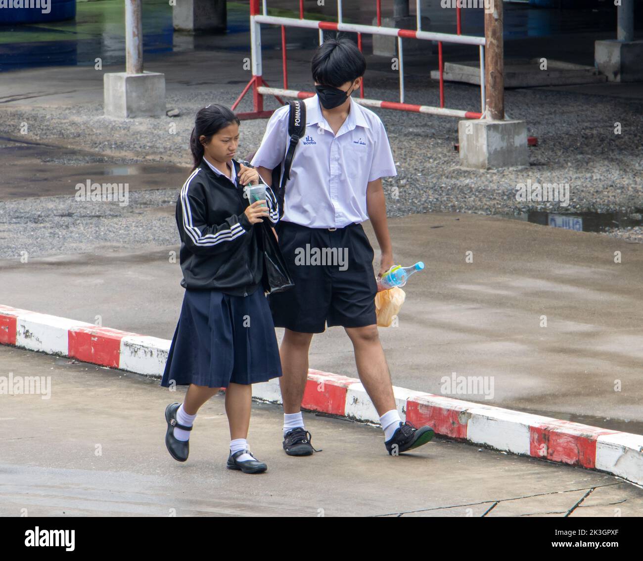 SAMUT PRAKAN, THAILAND, SEP 23 2022, A boy and a girl in school uniforms are walking on a wet street Stock Photo
