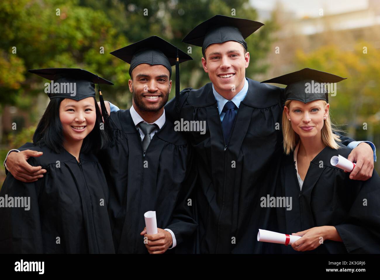 Difficult roads often lead to beautiful destinations. A group of college graduates standing in cap and gown and holding their diplomas. Stock Photo