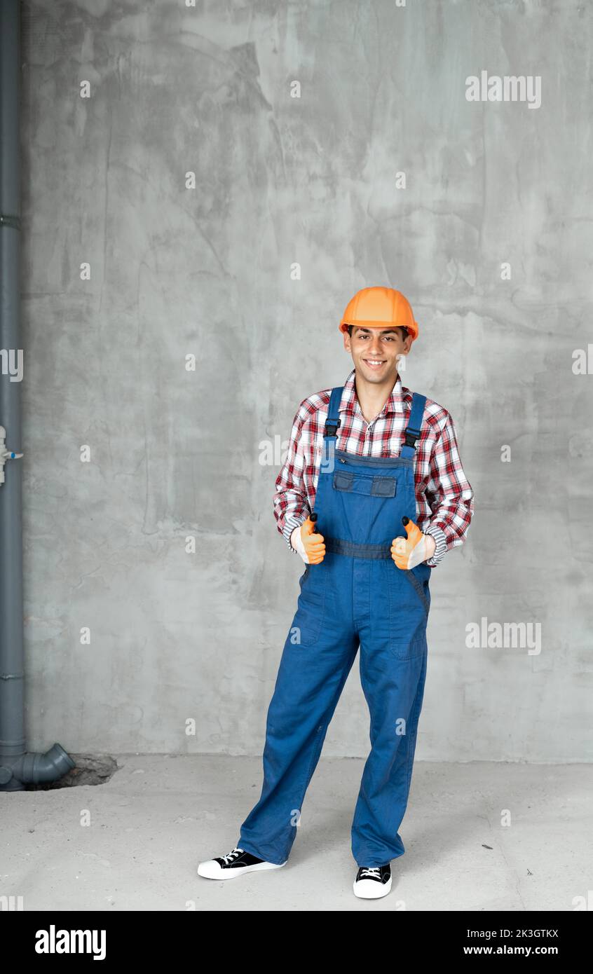 Young arabic man over grey concrete wall wearing contractor uniform and safety helmet happy with big smile doing ok sign, thumb up with fingers two ha Stock Photo
