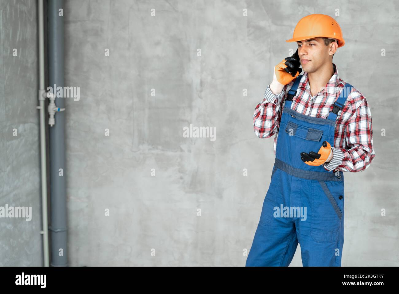 Professional arabic builder with safety helmet having a phone call on wall background, home renovation and communication concept Stock Photo