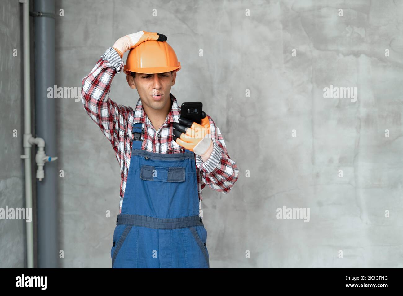 Photo of displeased negative young man builder in helmet posing isolated over gray wall background using mobile phone with app and bad sms. Stock Photo
