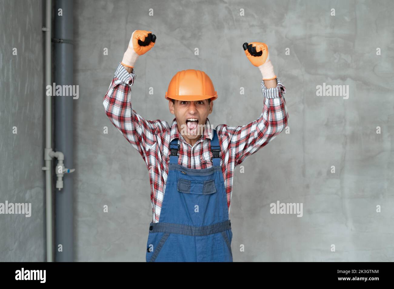 Angry builder man wearing construction uniform and safety helmet over gray wall background shouting and screaming with hands up. Communication and pro Stock Photo