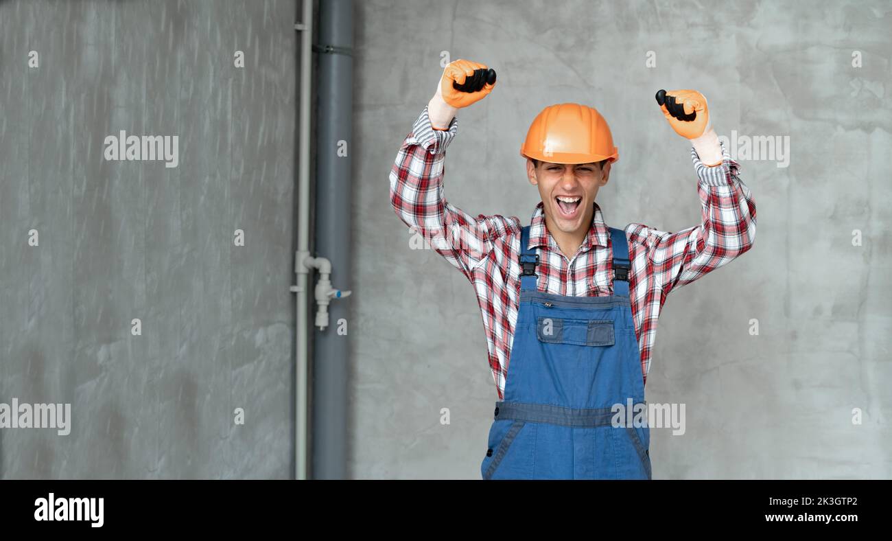 Photo of a happy positive young man builder in helmet posing isolated over gray wall background using mobile phone. profession, construction and build Stock Photo