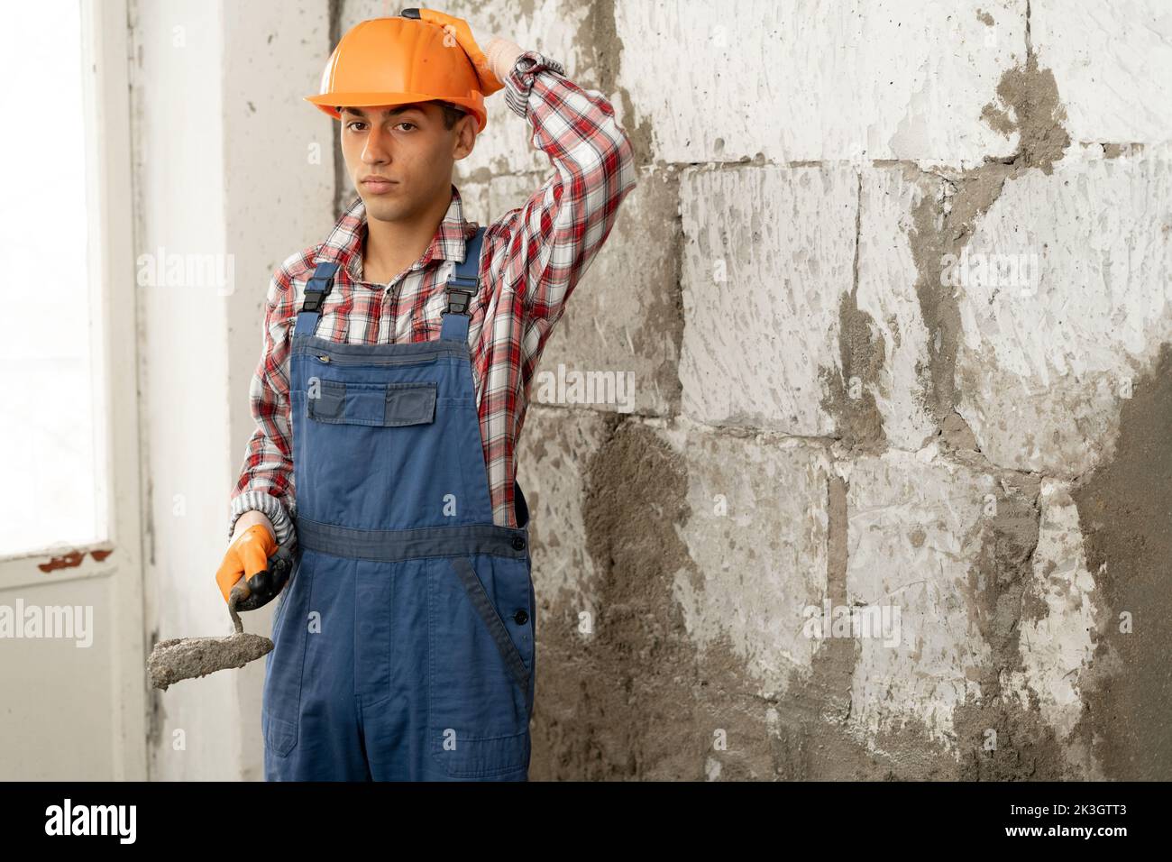 Thoughtful young builder with a spatula on the background of a wall of white bricks, making a wall with concrete mortar, a favorite profession, home r Stock Photo