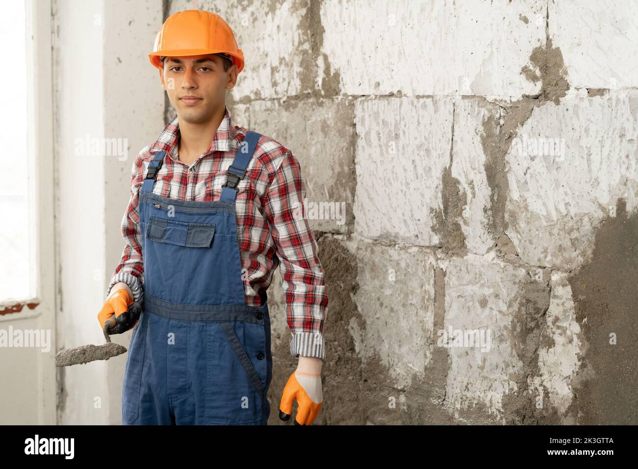 Arabic man master plasters the walls, portrait of builder in hard hat making repairs in the apartment, the concept of repairing and remodeling the hou Stock Photo