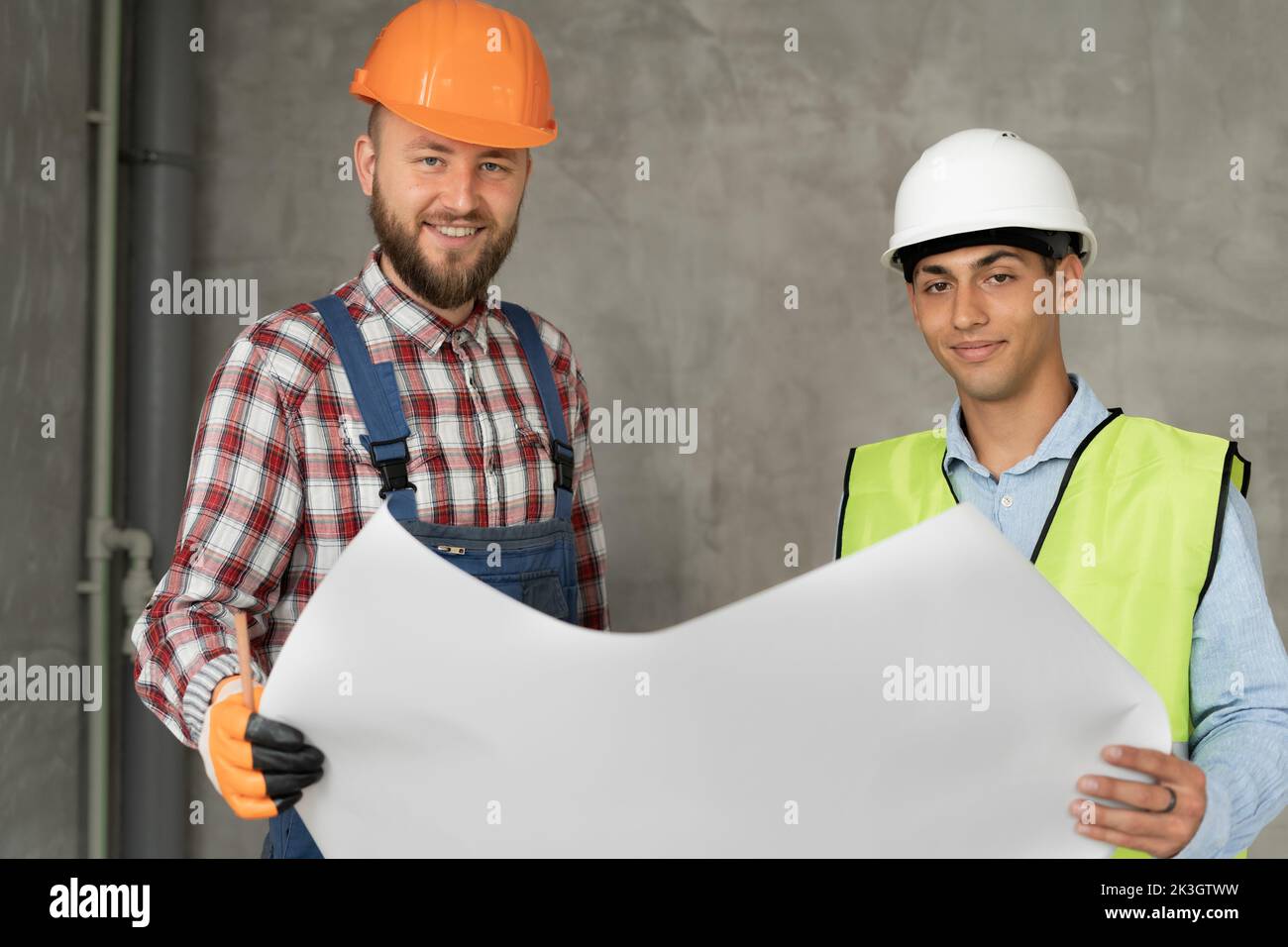 Happy architect and construction engineer or surveyor discussion plans and blueprints. Two men are wearing hardhats and are standing on the constructi Stock Photo