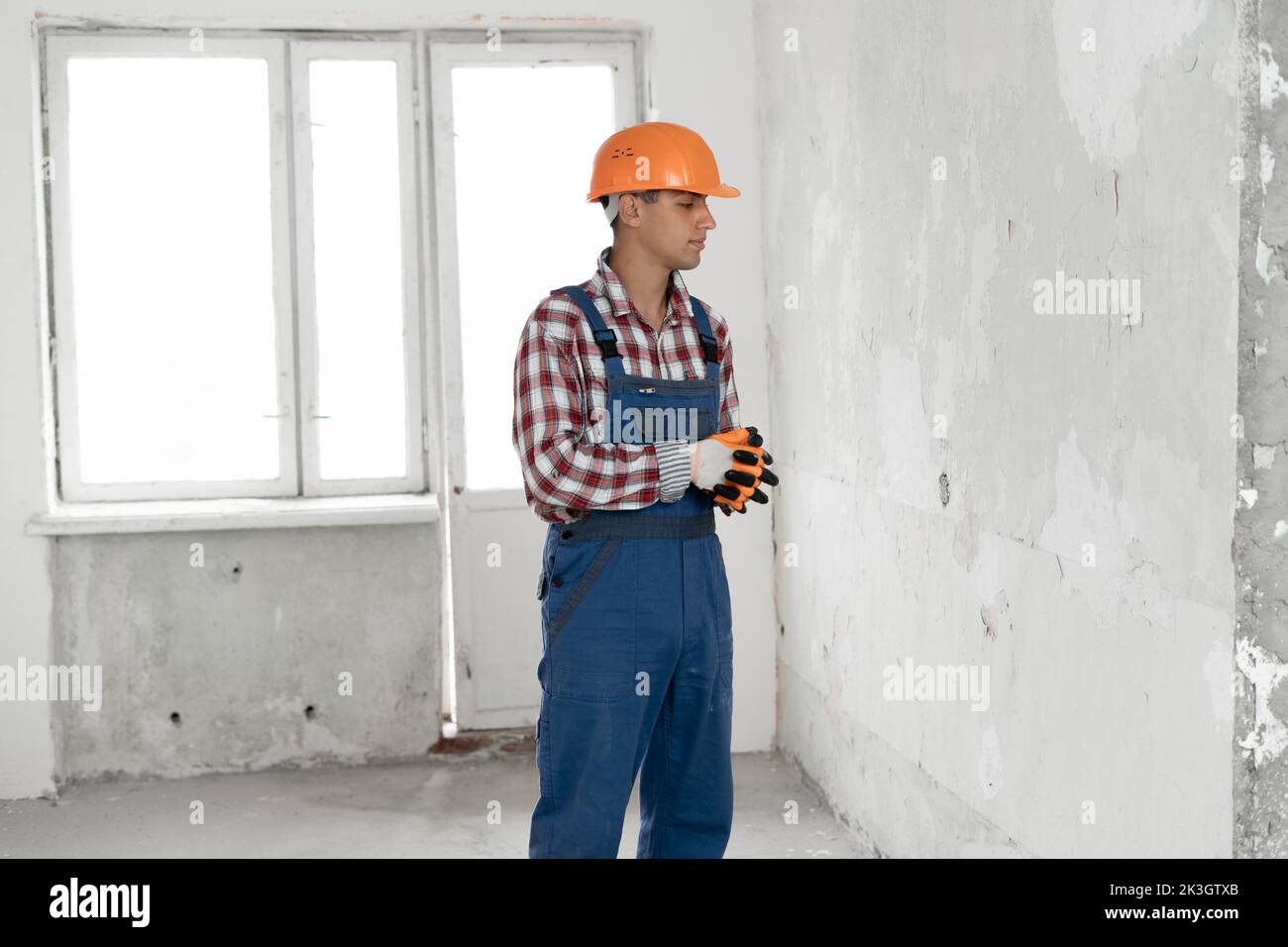 Full length portrait of a male builder in a helmet looking at gray wall background. repair, construction, building, people concept. space for text Stock Photo