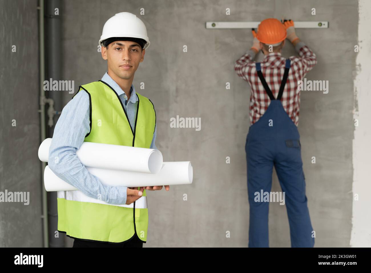 Architect man with blueprints and a working builder in the background against the wall, teamwork at a construction site. repair, building and remodeli Stock Photo