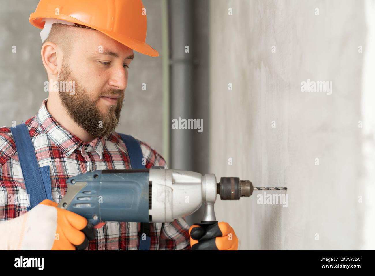 portrait of a young foreman working with a drill in the room, a builder drilling a wall makes repairs in the house, repair service and construction co Stock Photo