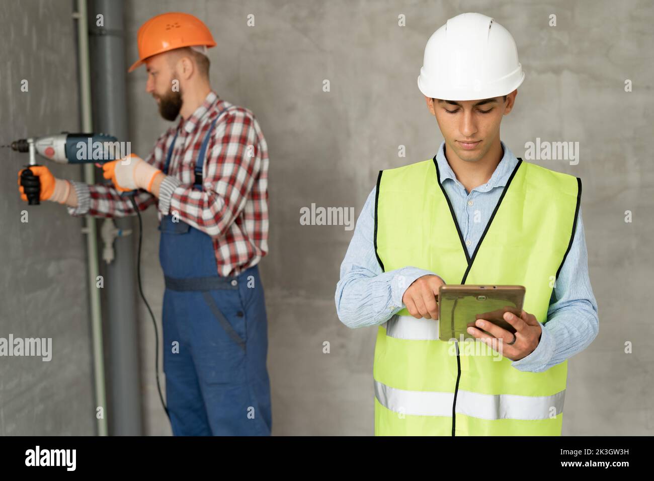 engineer or architector wearing safety jacket and helmets, inspecting project working with tablet computer on construction site. Construction worker w Stock Photo