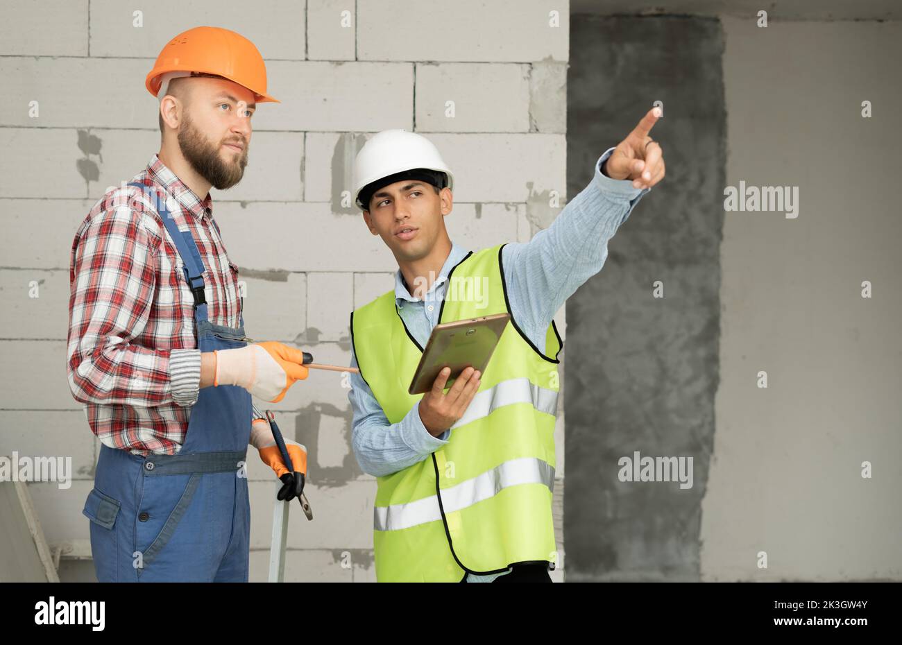 serious builders in hardhats with tablet computer indoors. business, building, teamwork, technology and people concept Stock Photo