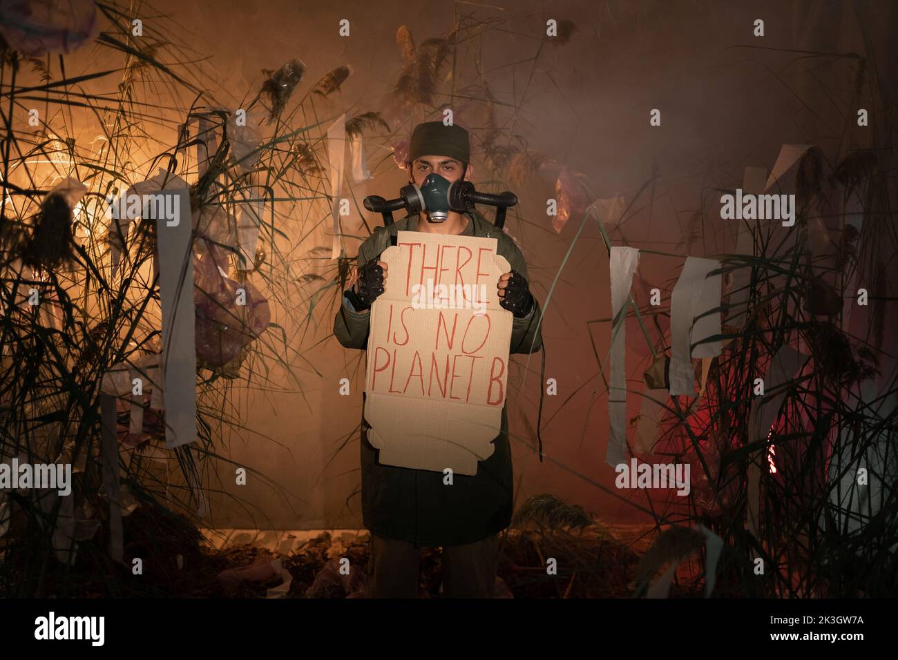 man in a gas mask holding poster with words there is No Planet B. burning plastic trash and smoke on background. concept of environmental problems Stock Photo