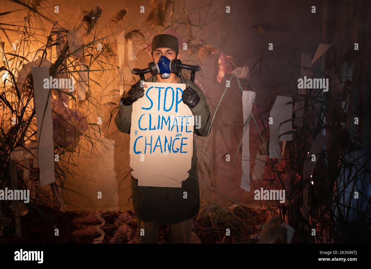 Environmental Protection. A man in a gas mask holds a poster with word stop climate change in smoke. Concept of environmental protection. Air pollutio Stock Photo