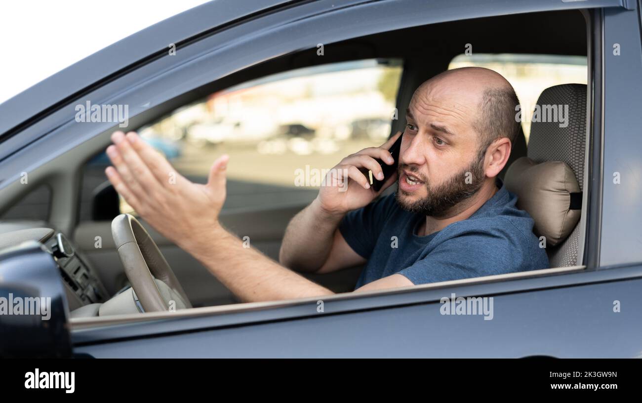 Man sitting in car with mobile phone calling while driving. Distracted shocked guy not paying attention at road using smartphone annoyed by bad news o Stock Photo