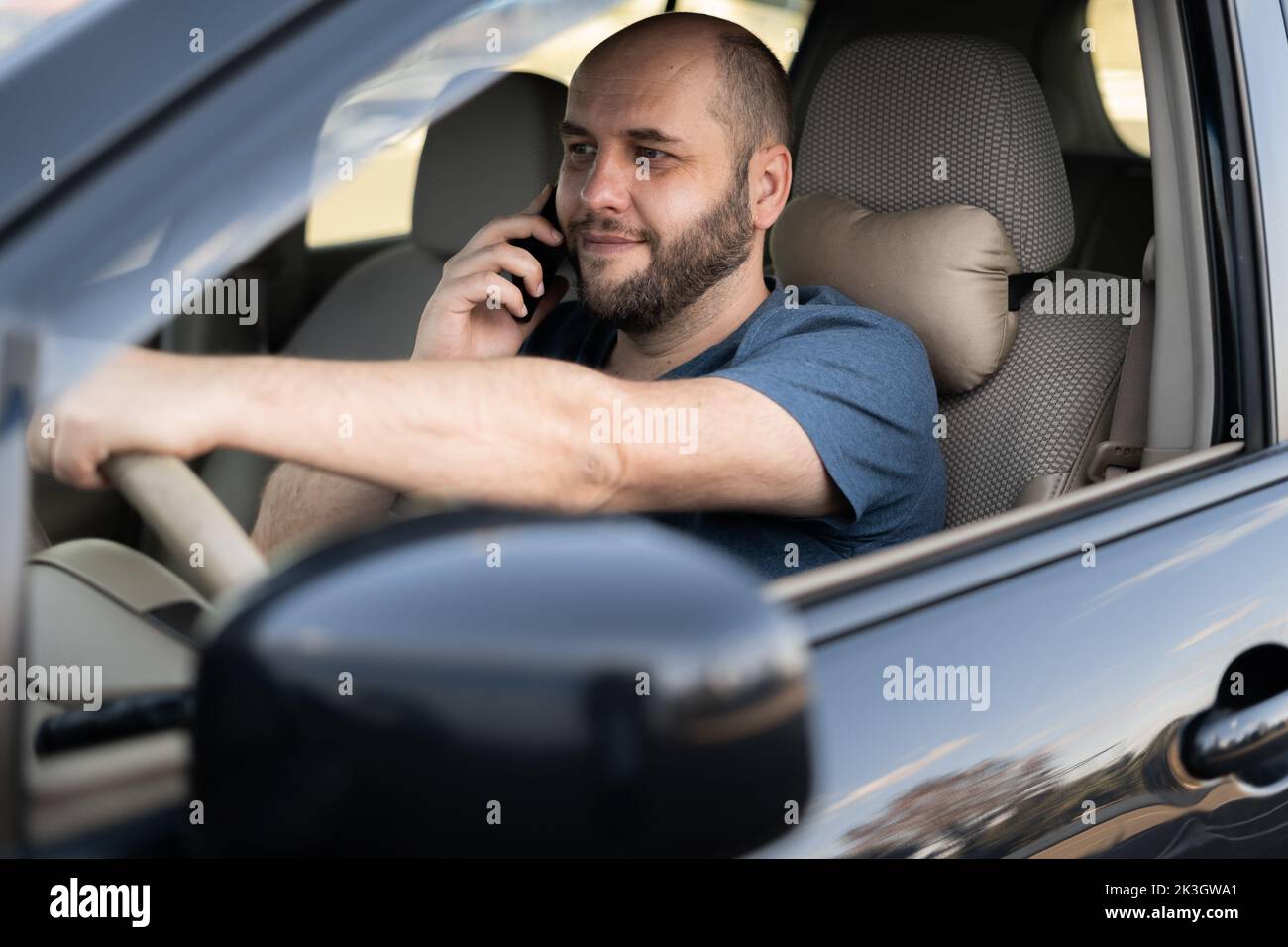 Portrait of smiling adult man driving car speaking on mobile phone. Stock Photo