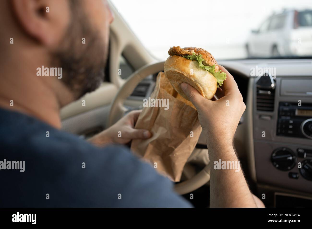 The driver eating a hamburger in the car. Breakfast burger in a traffic jam Stock Photo