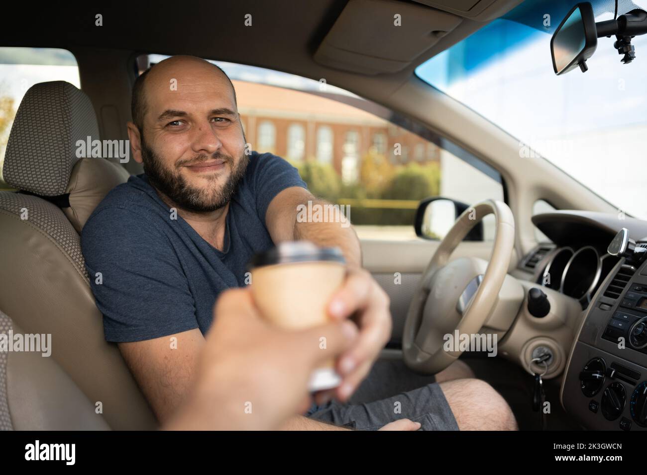 portrait of man sitting in car and buying coffee to go. Here you are. man driving his car and holding coffee while evincing joy Stock Photo