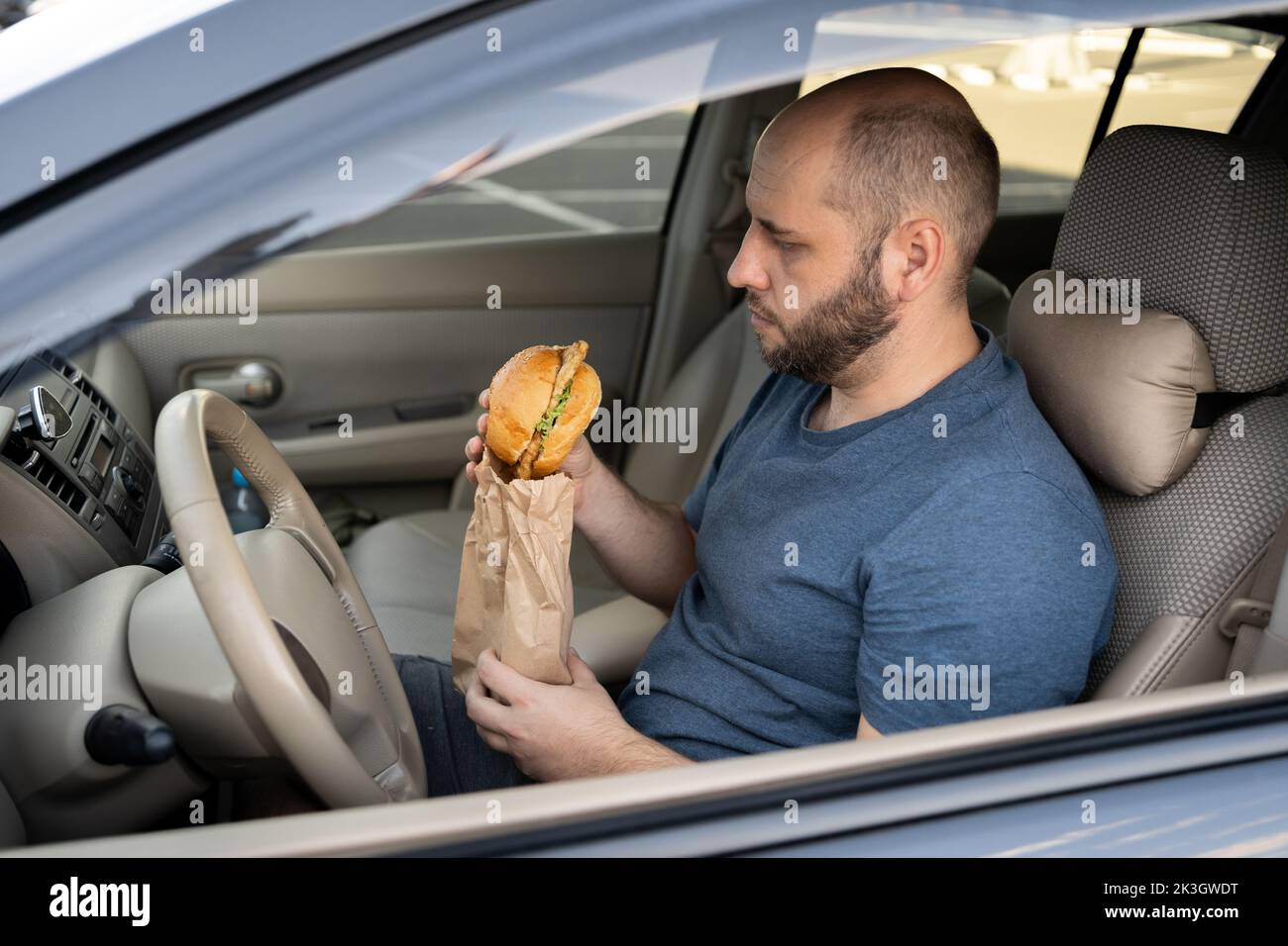 Man driving car while eating hamburger. Waiting and standing in traffic jam on road Stock Photo