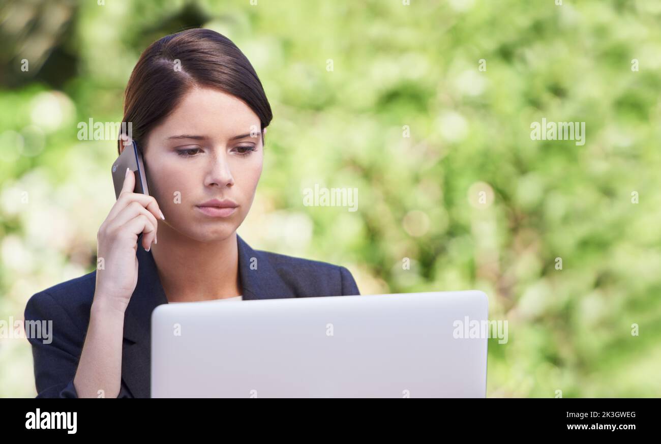 This is unacceptable. A serious-looking young woman talking on a cellphone while using her laptop. Stock Photo