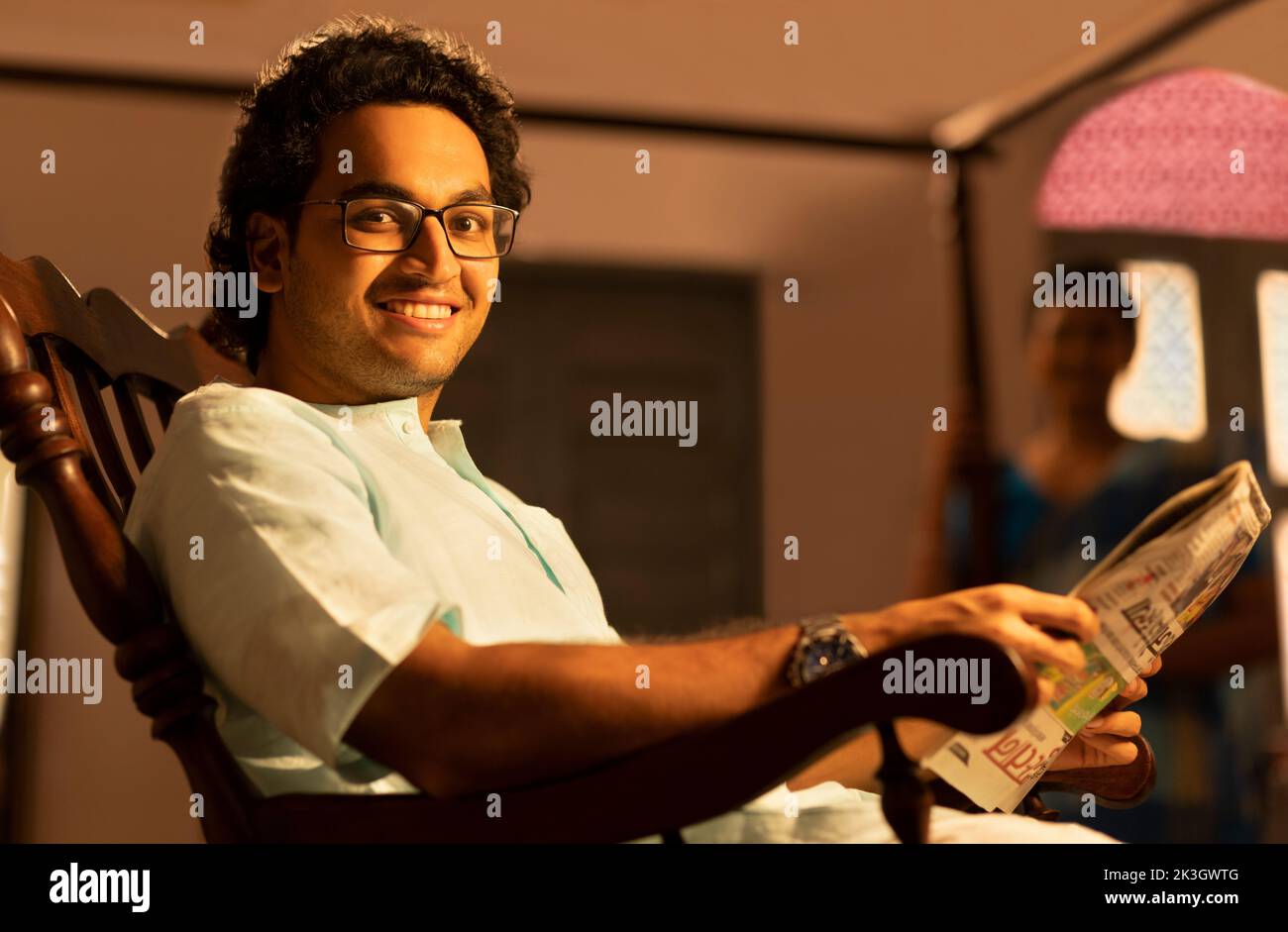 Portrait of Bengali man reading newspaper at home and wife standing away Stock Photo