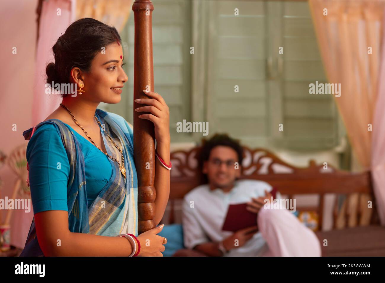 Portrait of Bengali woman standing and husband lying away on bed Stock
