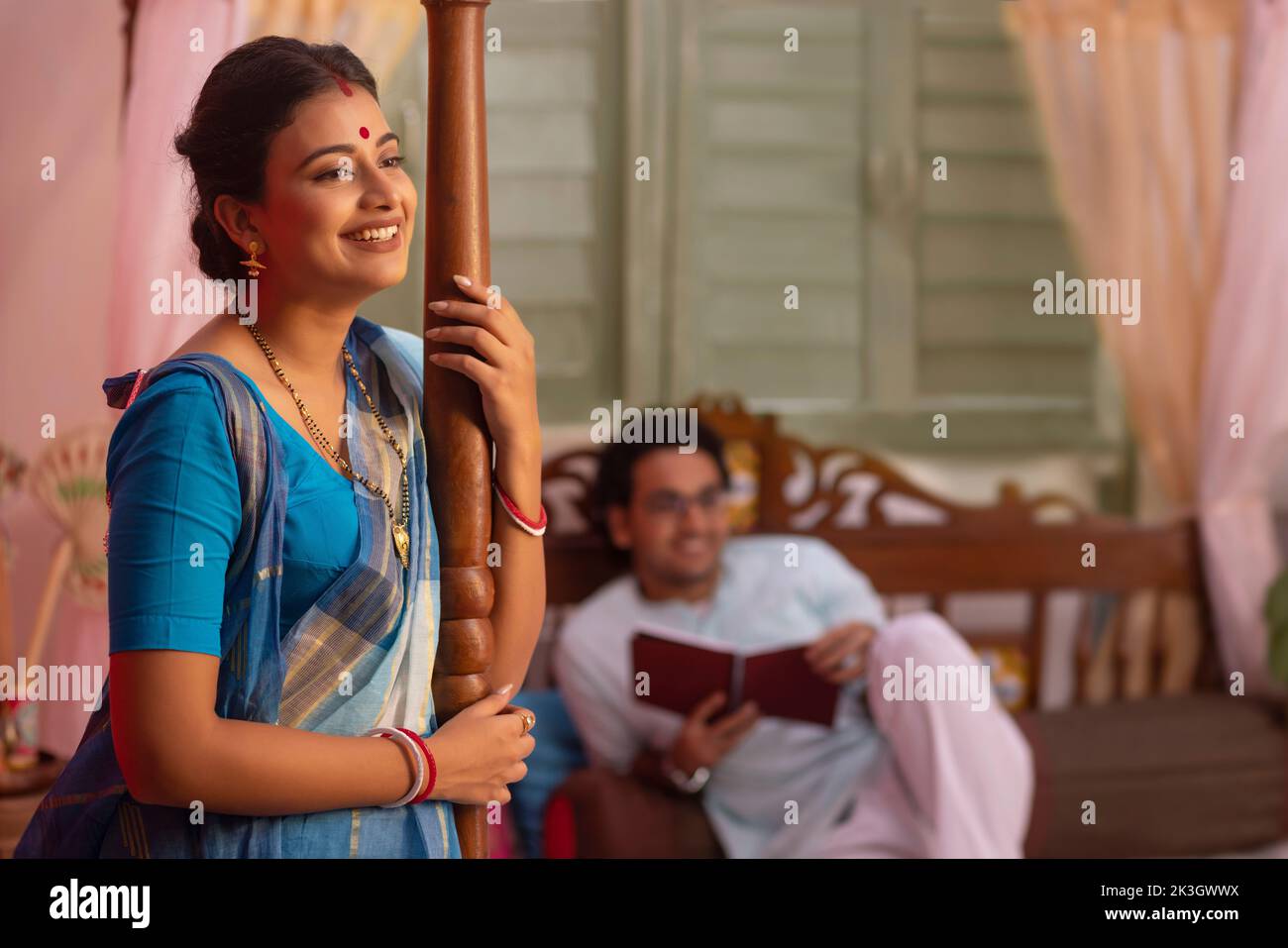 Portrait of Bengali woman standing and husband lying away on bed Stock