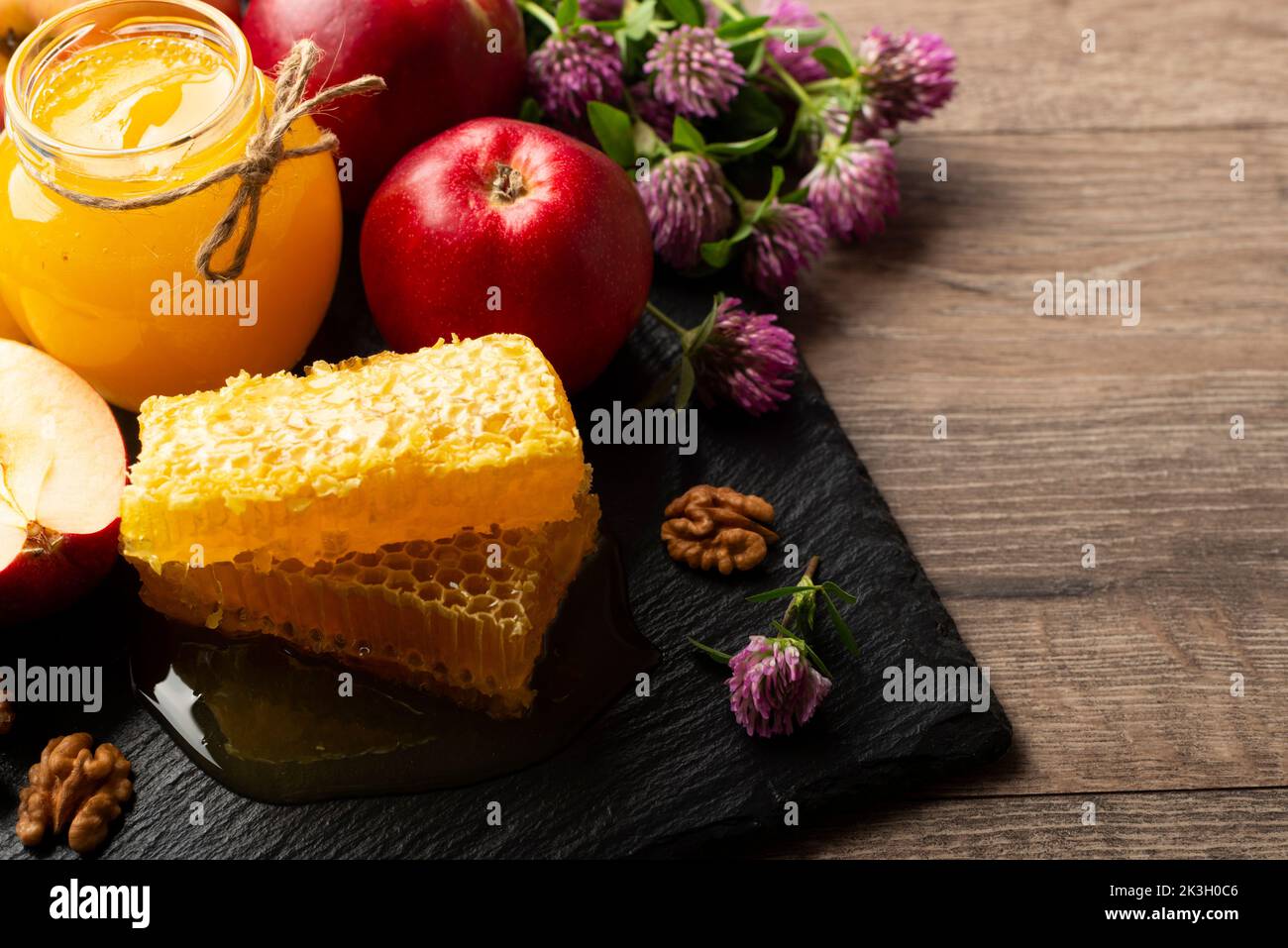 Mason jar with honey, honeycomb, red apples and walnuts on kitchen table Stock Photo
