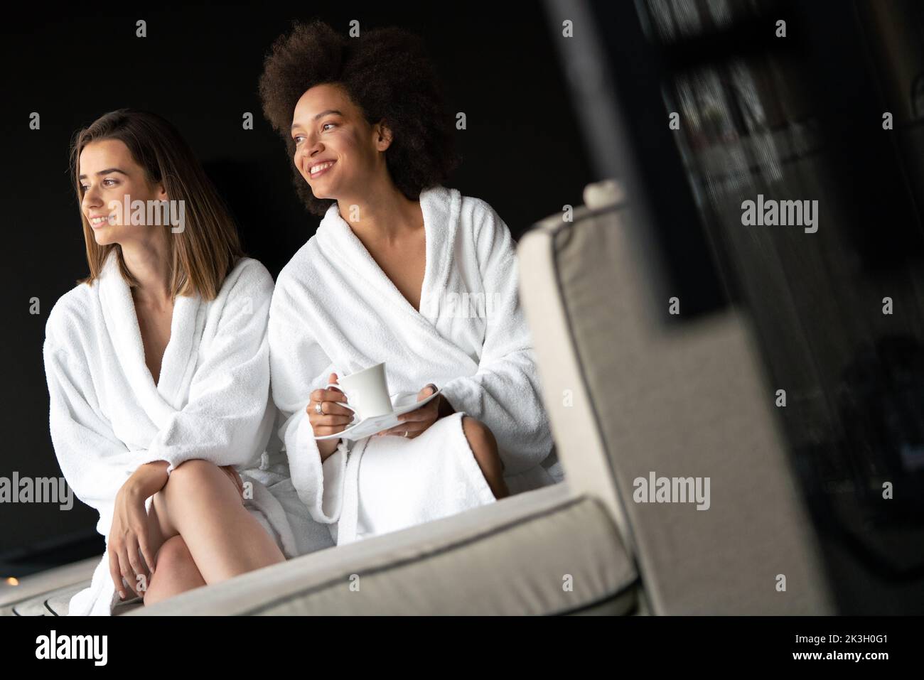Lesbian couple relaxing and drinking tea in robes during wellness weekend Stock Photo