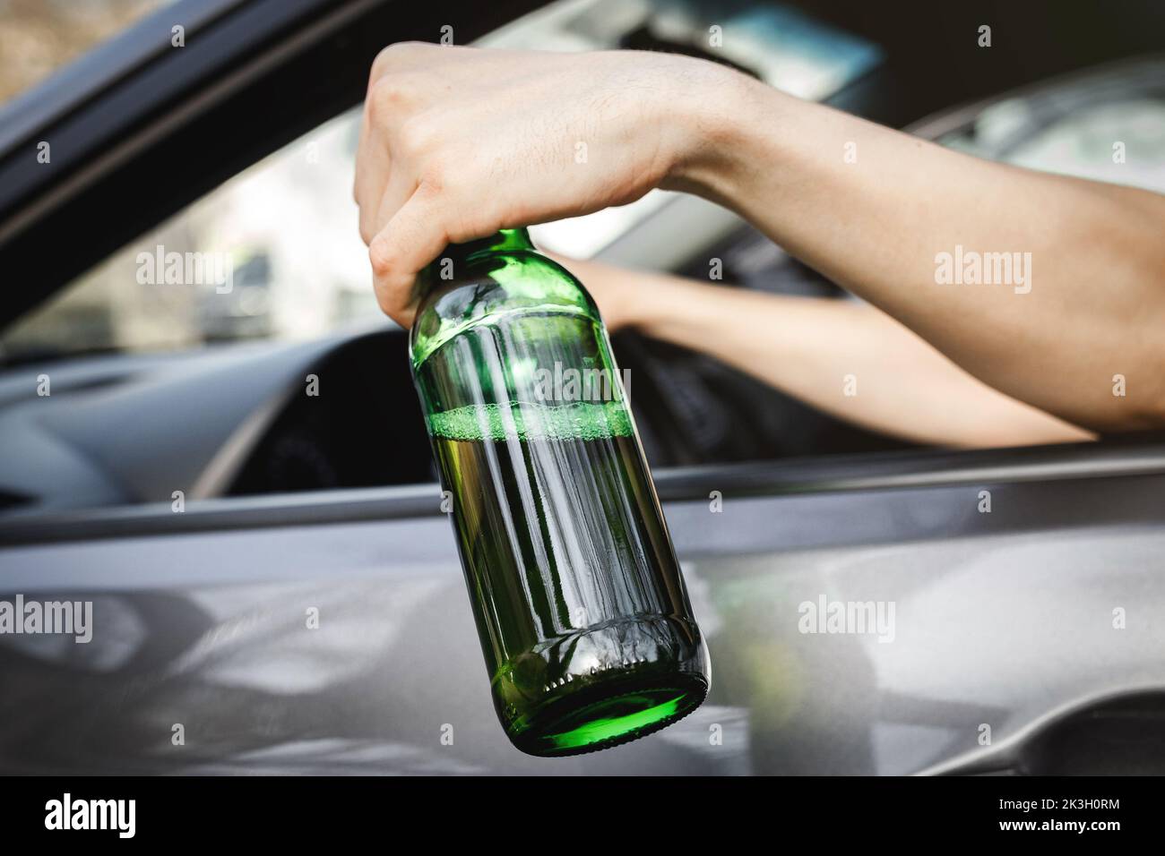 The driver's hand in the car window holds a bottle of alcohol Stock
