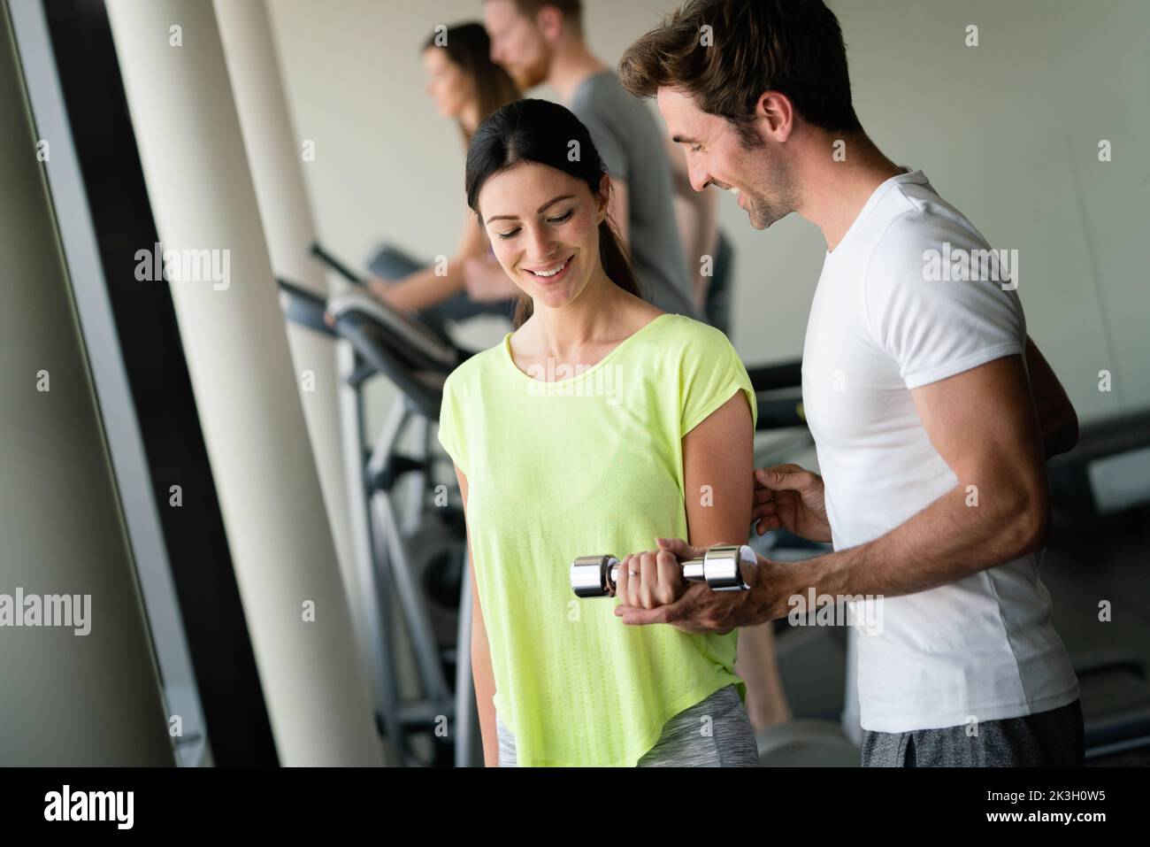 Man trainer flirting with beautiful young woman while helping her at gym Stock Photo