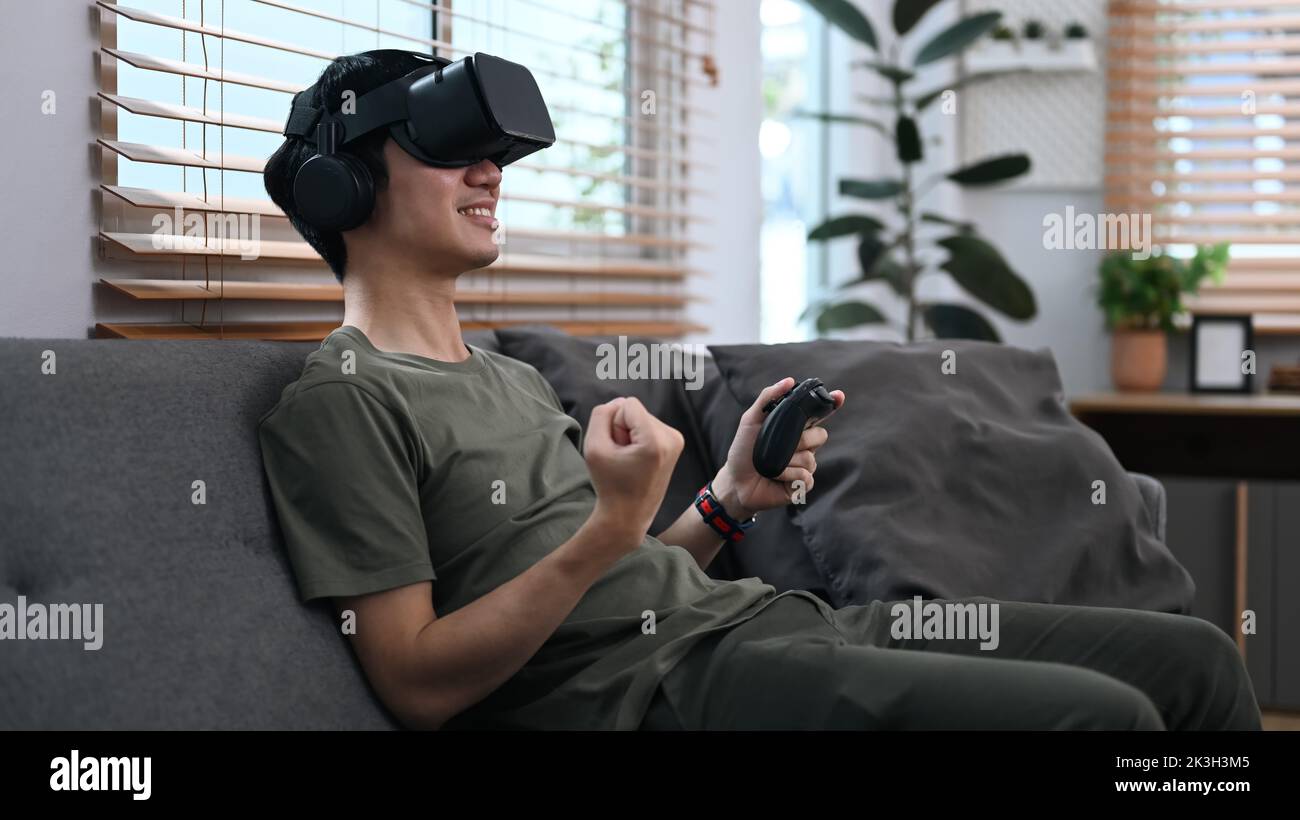 Joyful asian man wearing virtual reality headset, playing simulation boxing game in living room
