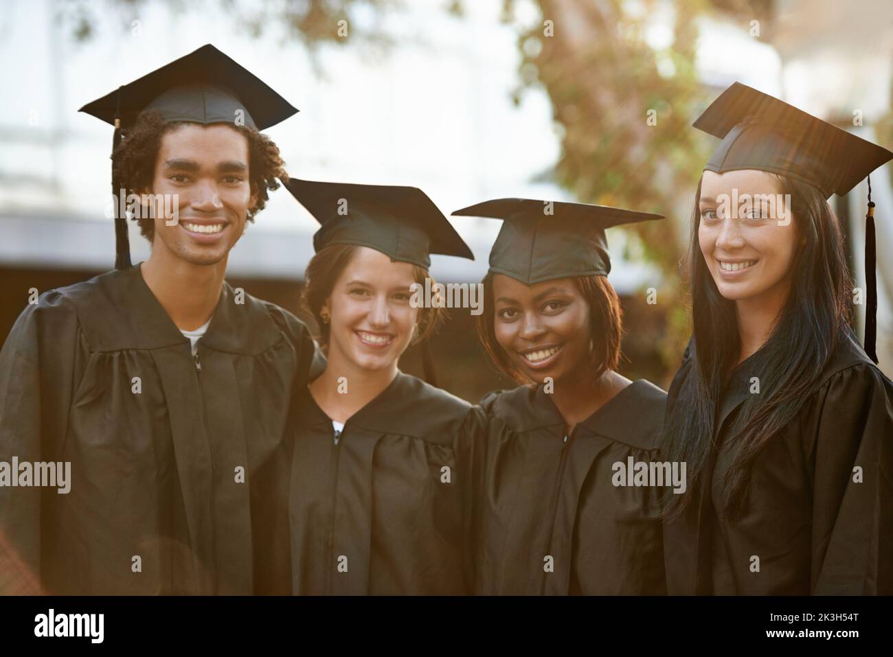 Proud to be graduates. A group of smiling college graduates standing together in cap and gown. Stock Photo