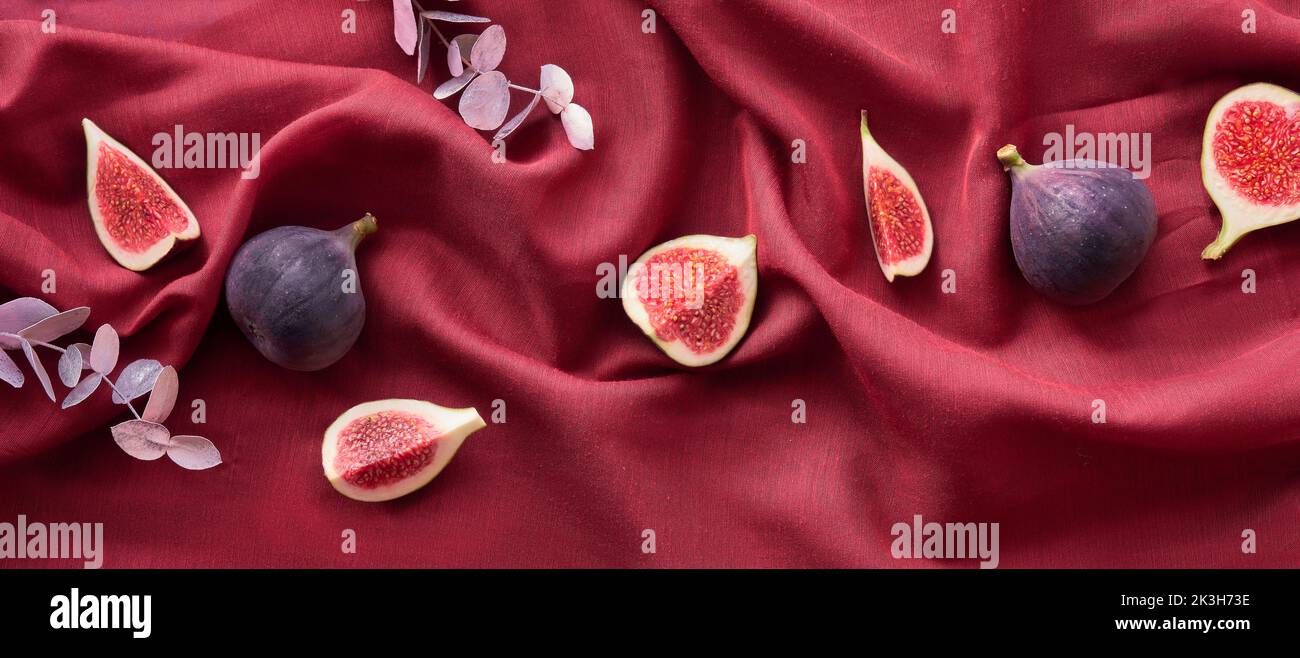 Fresh halved fig fruits and dry euvalyptus on vine red silk textile background. Panoramic banner Autumntime image. Stock Photo