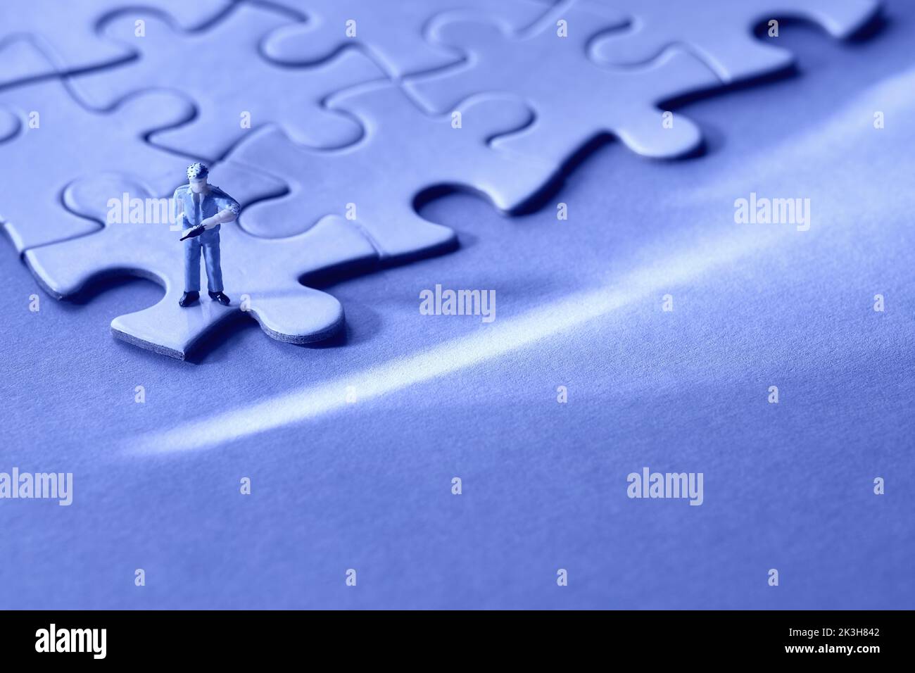 Concept of quiet quitting, job burnout, depression. Blue monochrome background. Single tiny worker miniature figure on edge of linked jigsaw puzzle Stock Photo