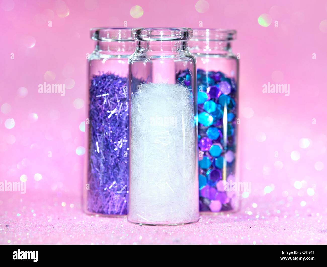 All kinds of glitter products on pink sparkling background. Close-up on vials, bottles with various glitter makeup in neon pink, blue and turquoise. Stock Photo