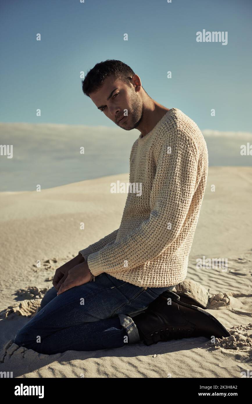 Man vs. desert. Handsome man kneeling on the desert sand in trendy clothing. Stock Photo