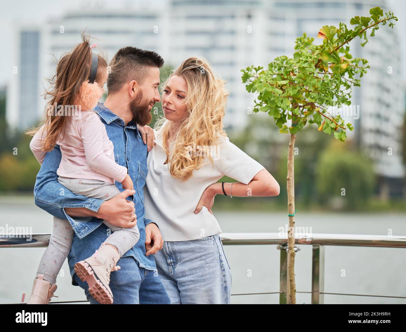 Man and woman with child outdoors. Father holding adorable child while spending time with family in new urban district. Stock Photo