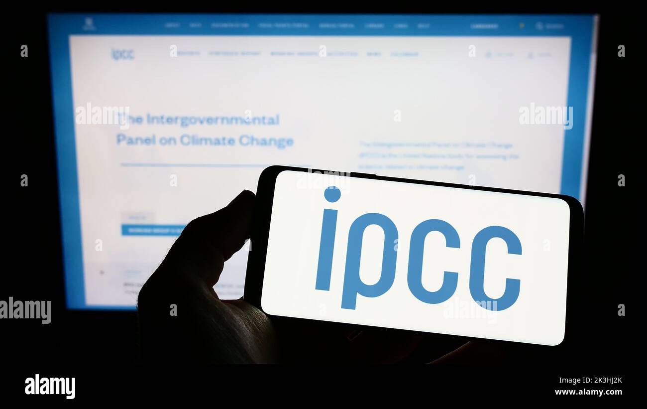 Person holding smartphone with logo of Intergovernmental Panel on Climate Change (IPCC) on screen in front of website. Focus on phone display. Stock Photo