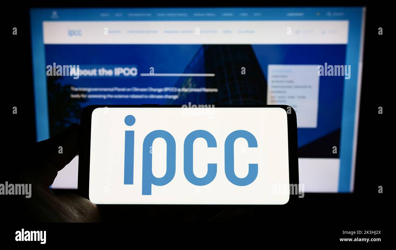 Person holding mobile phone with logo of Intergovernmental Panel on Climate Change (IPCC) on screen in front of web page. Focus on phone display. Stock Photo