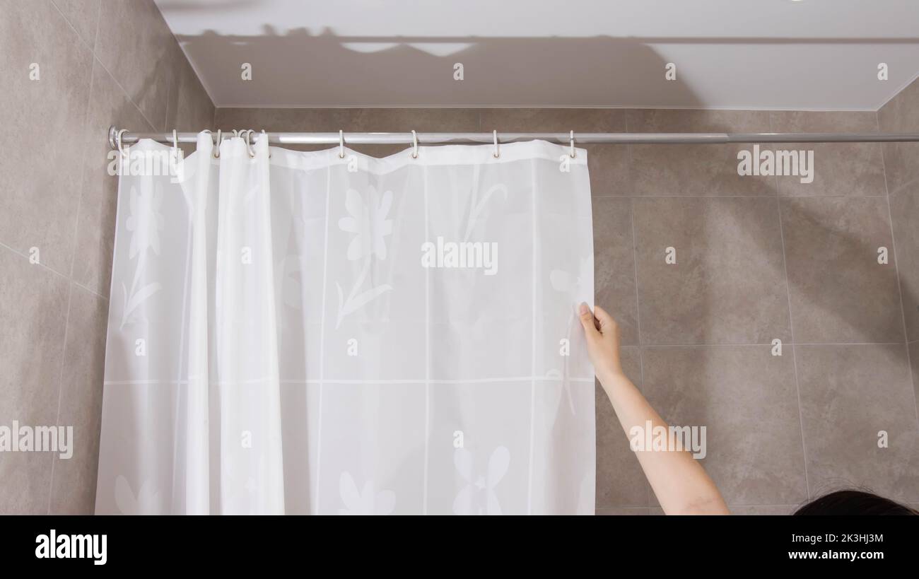 A man opens a shower curtain in the bathroom to protect against