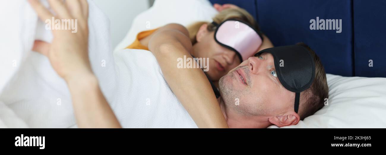 Dumbfounded man wakes up at night from nightmare next to woman Stock Photo