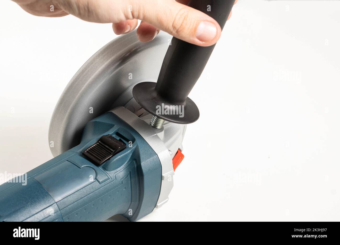 The hand twists the extra handle into the angle grinder for a