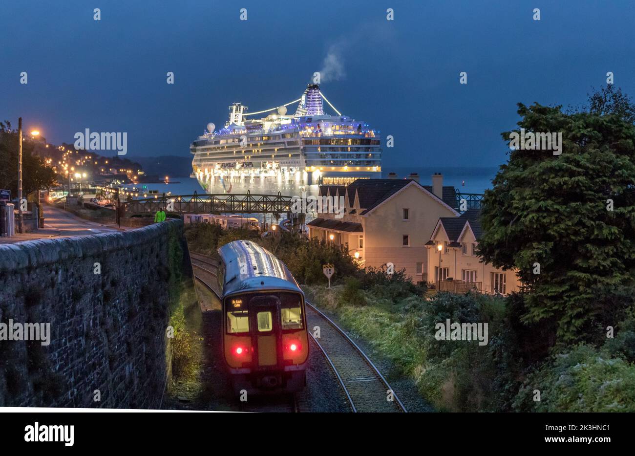 Cobh, Cork, Ireland. 27th September, 2022. An early morning commuter train approaches the station as the cruise ship Norwegian Dawn arrives to her berth in Cobh, Co. Cork, Ireland. - Picture David Creedon Stock Photo