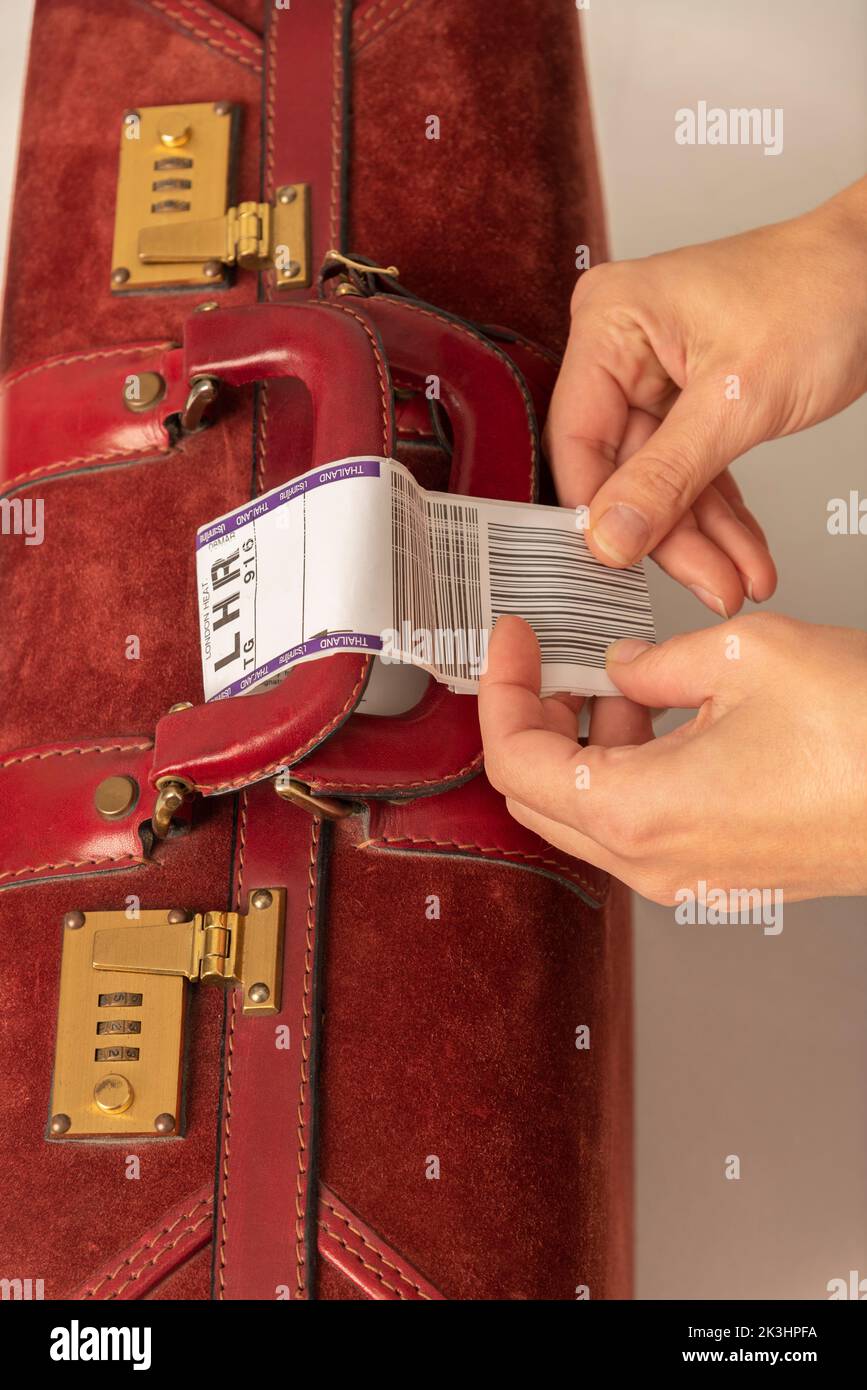 Enngland, UK. 2022. Airline luggage destination identity tag being attached to a dark red leather suitcase handle by womans hands. Stock Photo