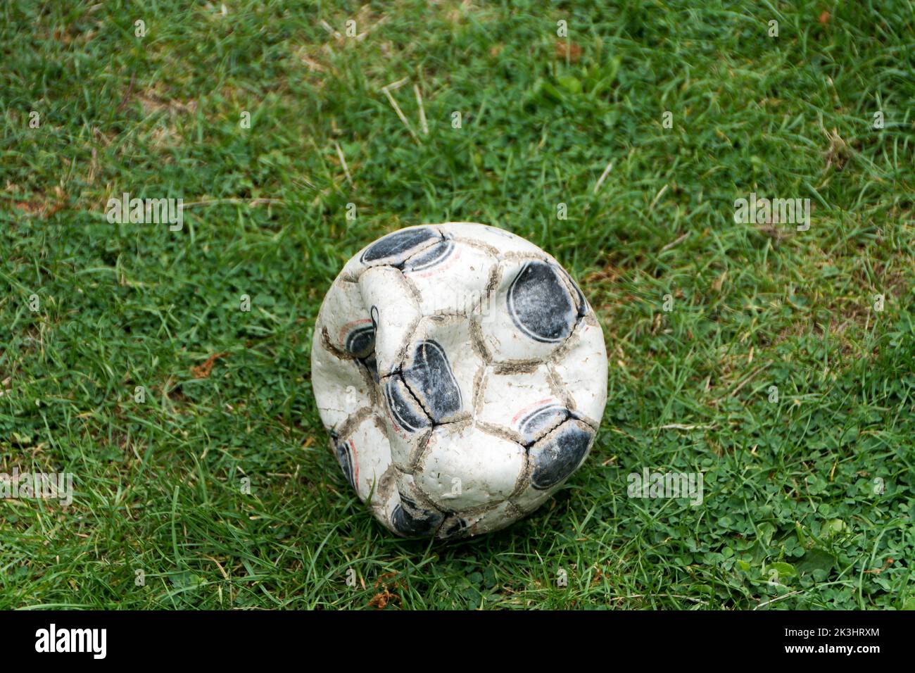 Beaten up old blue and white football not fully inflated on a background of green grass - perfect for any number of different messages. Soft. Stock Photo