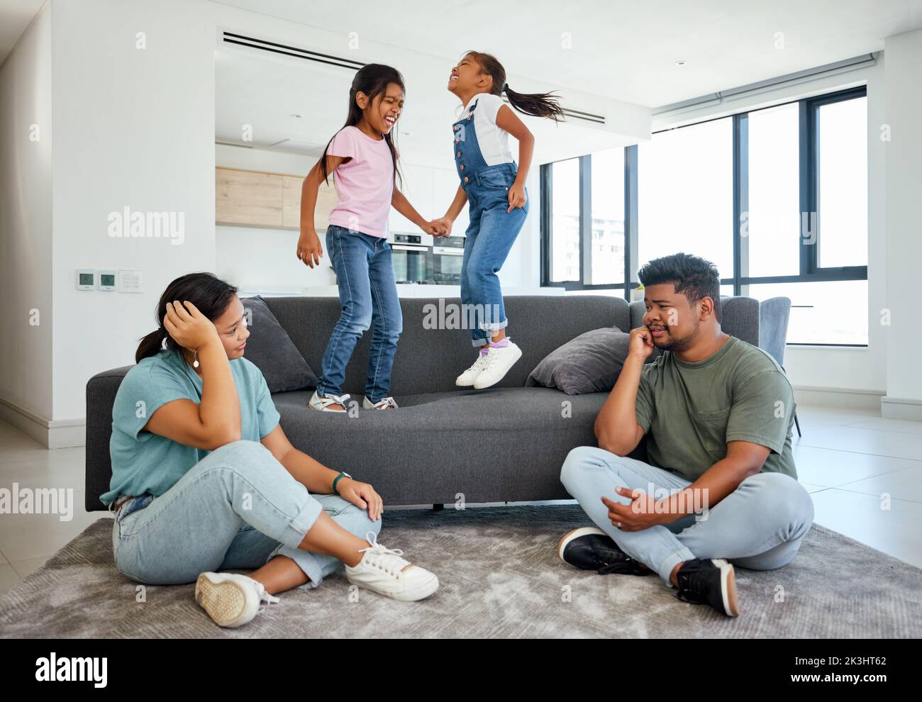 Family, energy and kids jumping on home sofa with tired parents struggling with naughty, hyperactive and playing children. Woman and man with ADHD Stock Photo