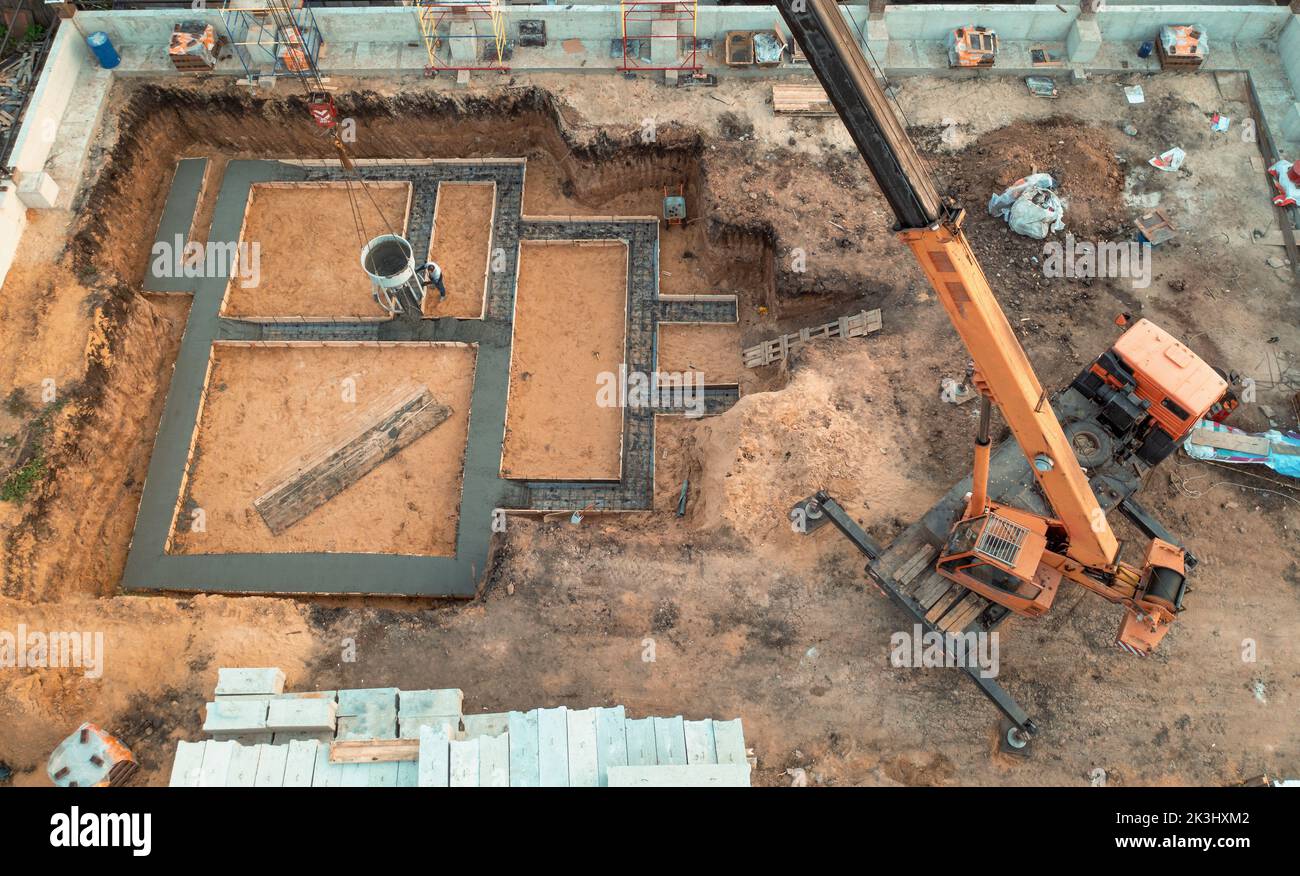 Foundation of future house. Pouring foundation with cement on construction site with crane, aerial view. Stock Photo