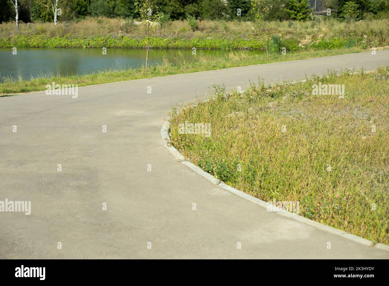 Road in park. Asphalt path and green lawn. Improvement of park. Place for walking. Empty path. Stock Photo