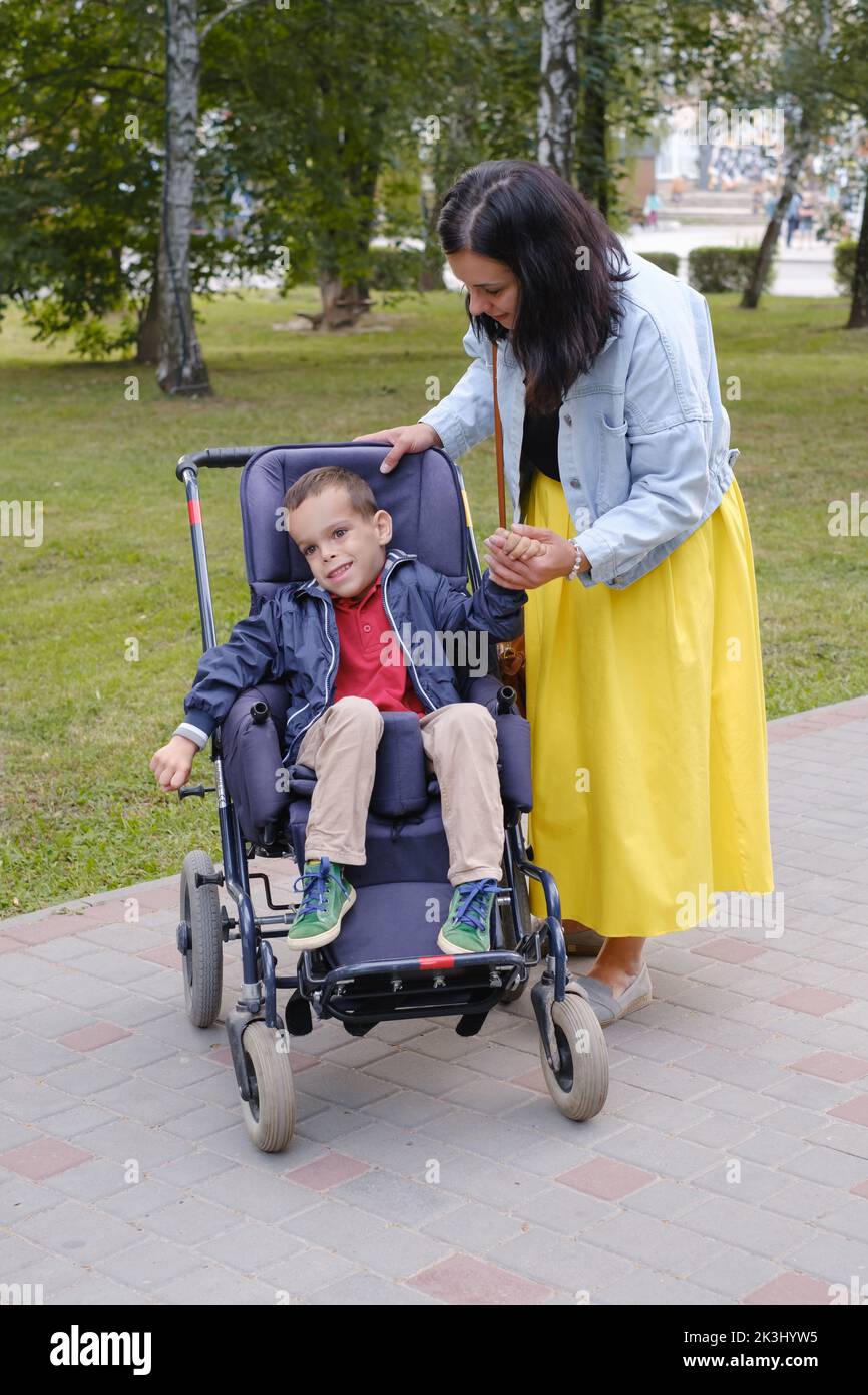 Family with cerebral palsy child on special wheelchair walking outdoors. Integration and accessibility of disabled people, inclusion. Brother with Stock Photo