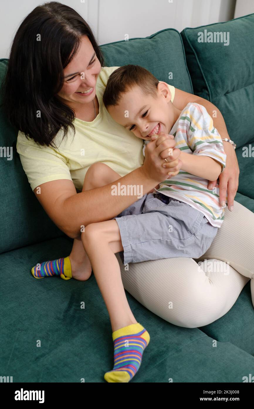 Mother with disabled child on sofa. Woman hugging boy with cerebral palsy at home. Mother having fun, taking care of handicap boy Leisure time Stock Photo